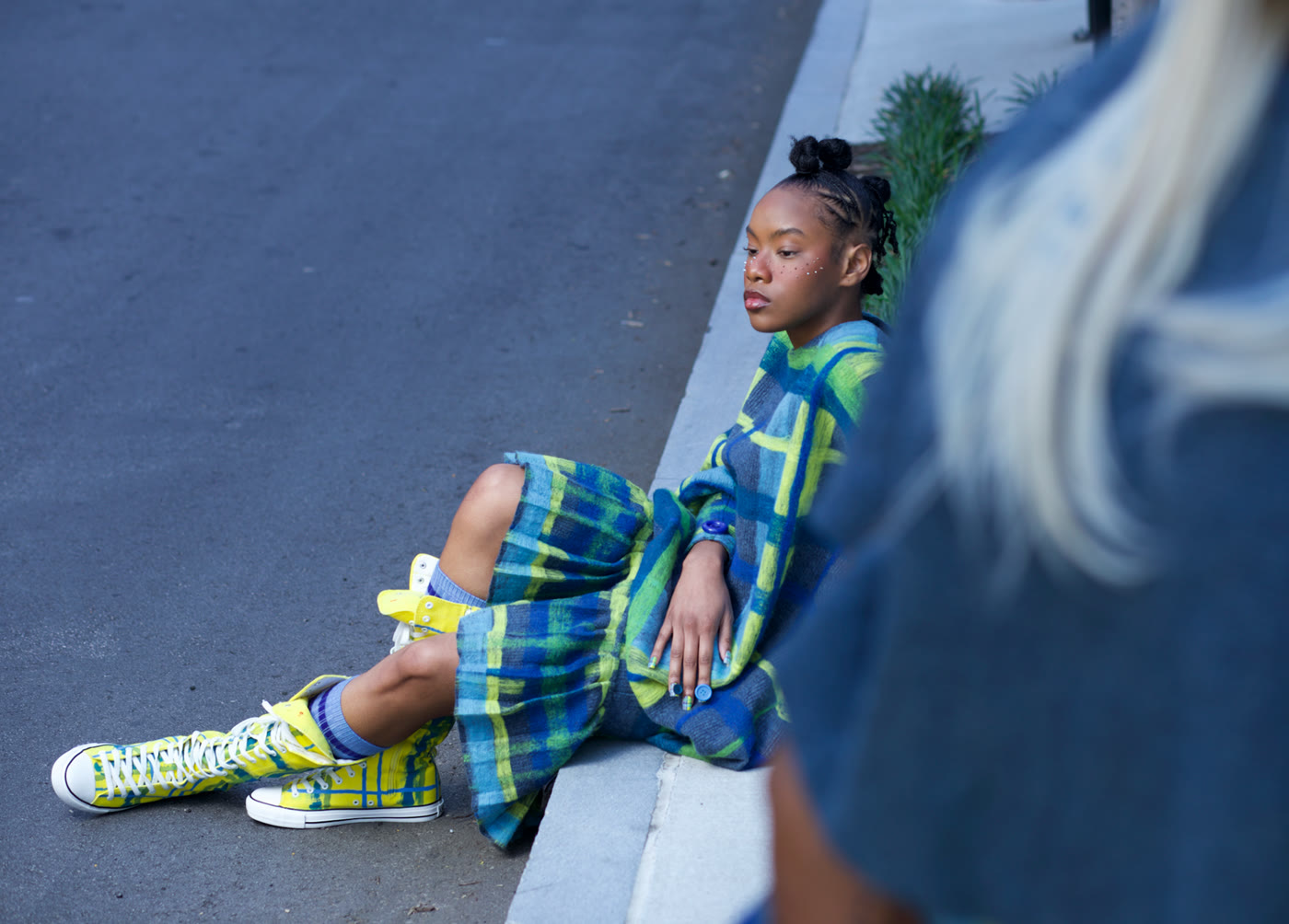Editorial photograph — model seated on concrete steps in plaid and hi-tops